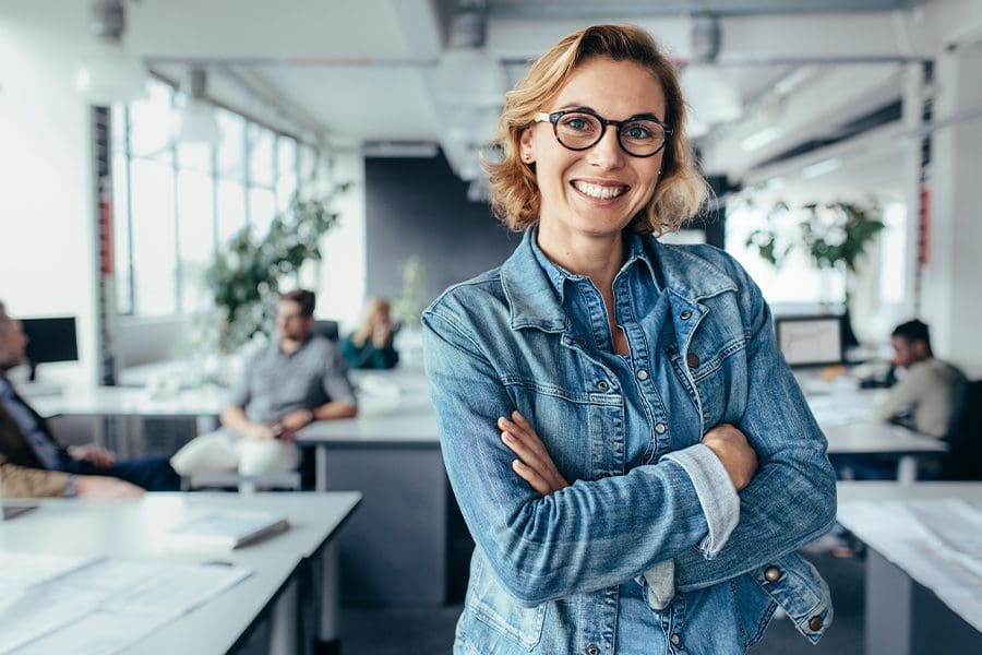 Business Insurance - Happy Businesswoman Standing in the Office with Background and Coworkers Blurred